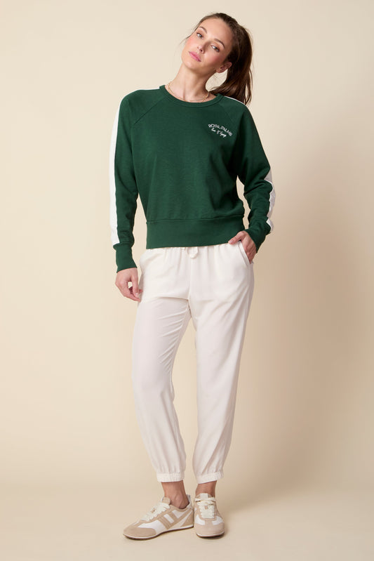 Woman wearing a green sweater and white pants against a beige background