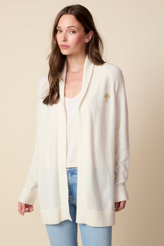 Woman wearing a white cardigan over a white top and blue jeans on a beige background