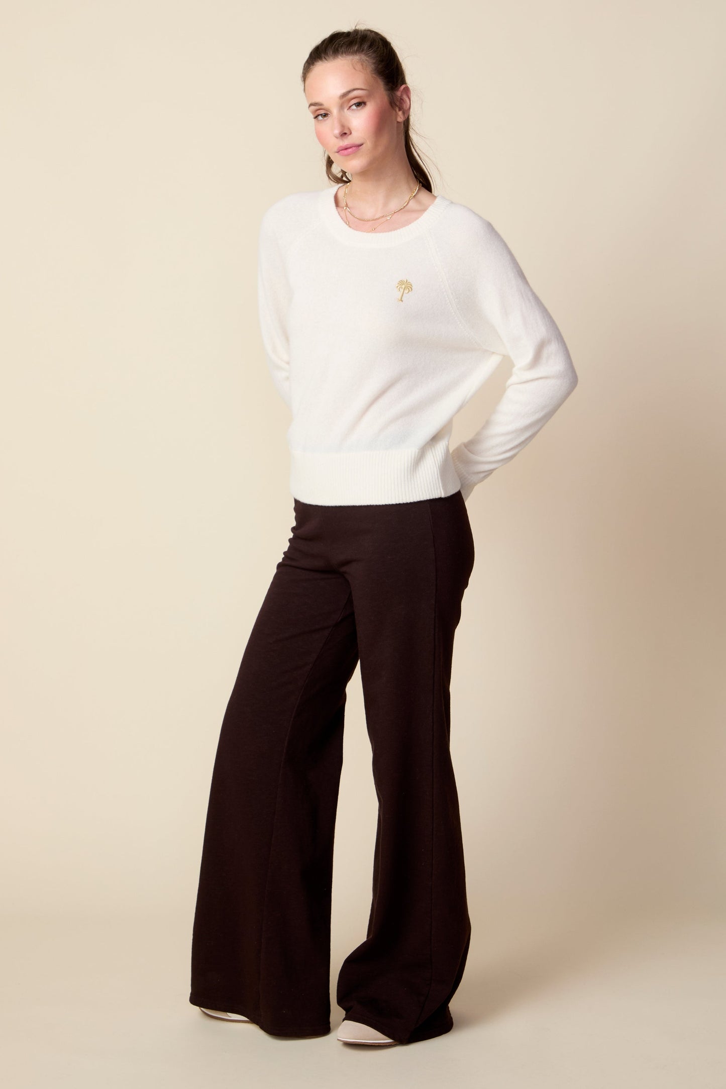 Woman wearing a white sweater and brown pants on a beige background