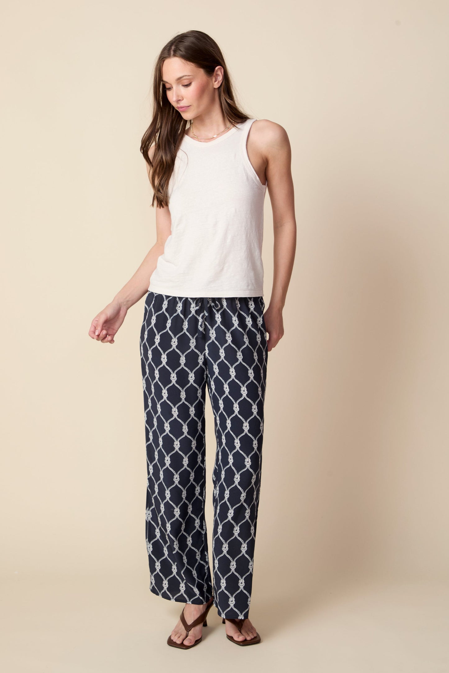 Woman wearing a white sleeveless top and patterned pants on a beige background