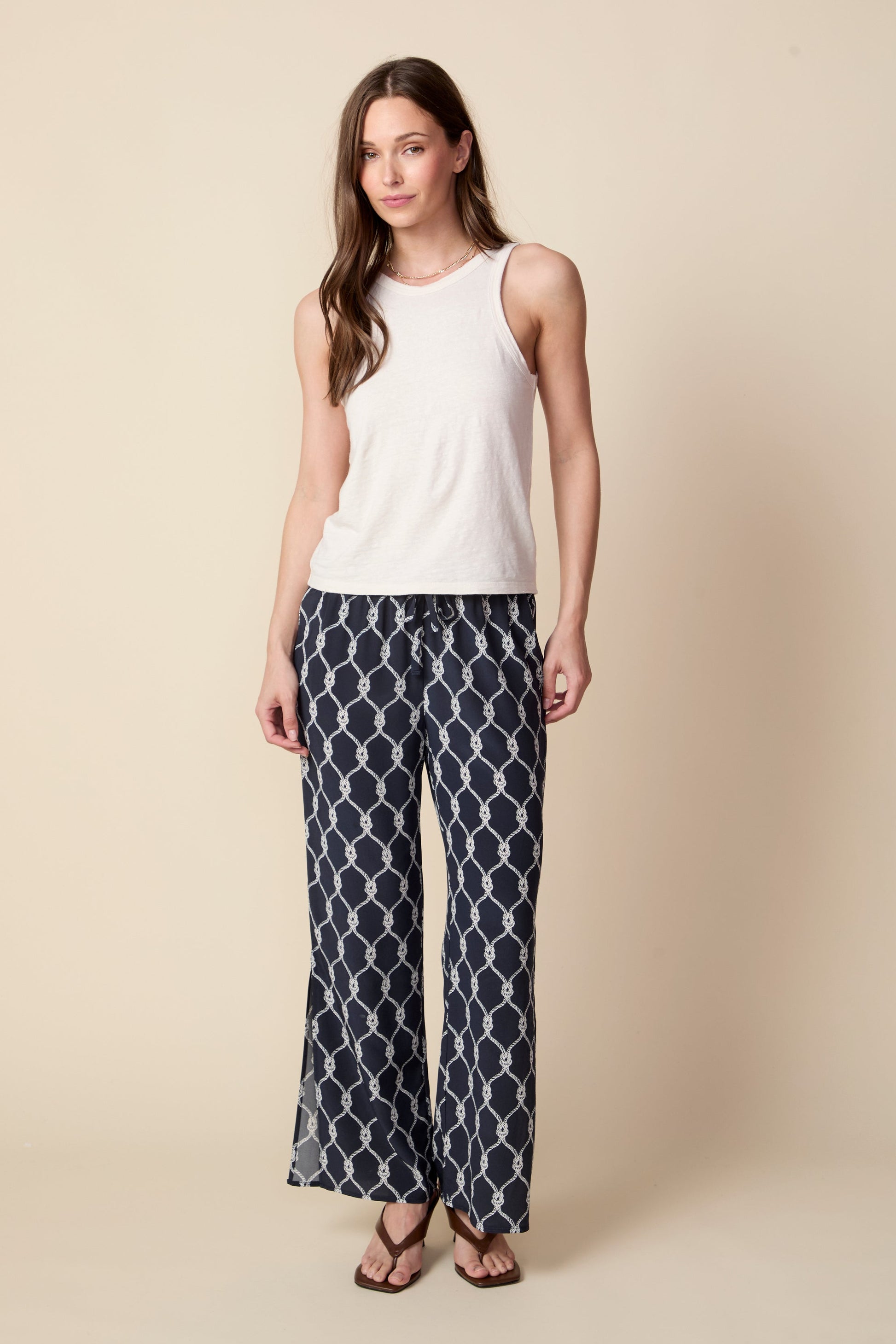 Woman wearing a white sleeveless top and patterned pants on a beige background