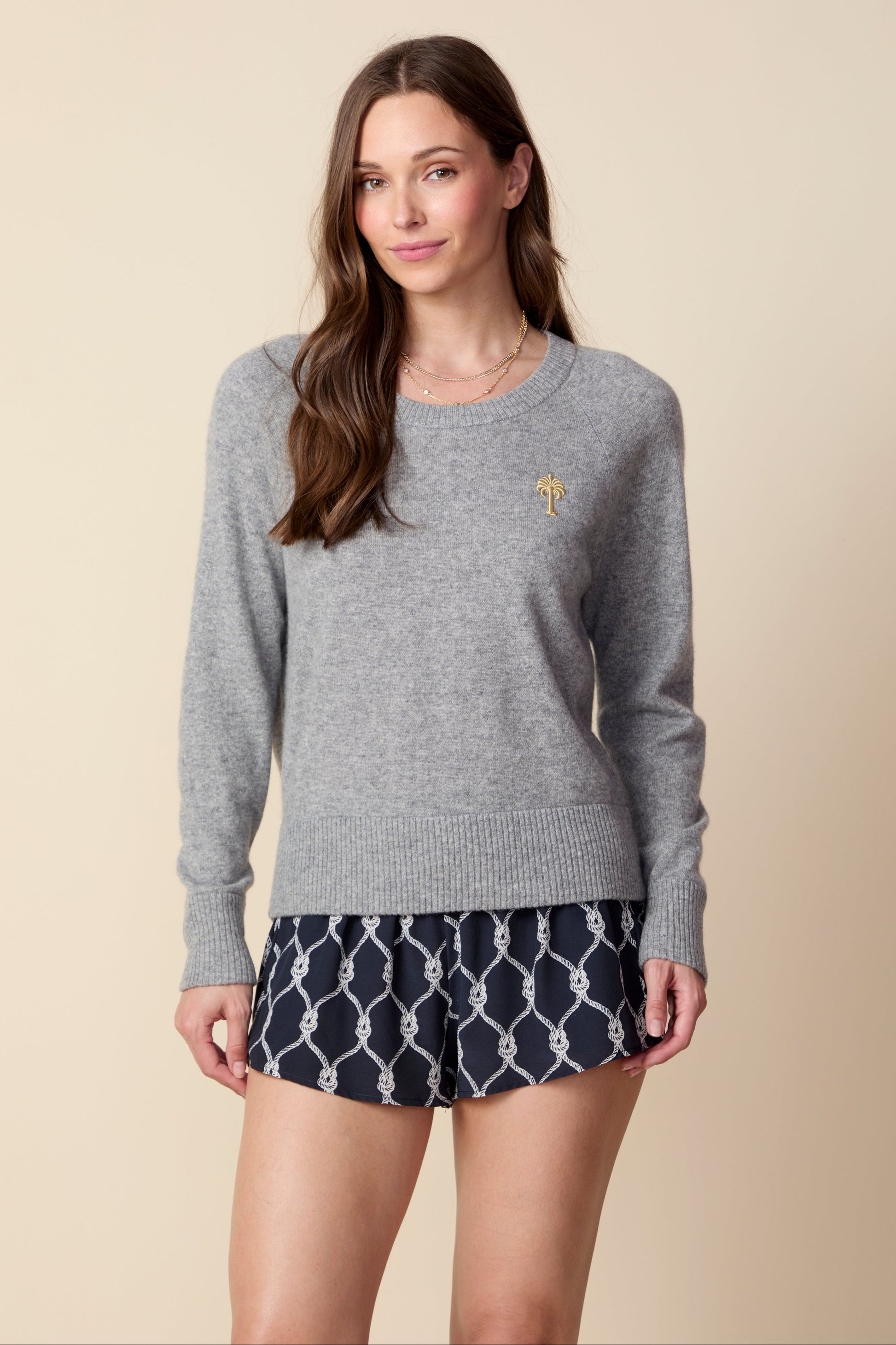 Woman wearing a gray sweater and patterned skirt on a beige background
