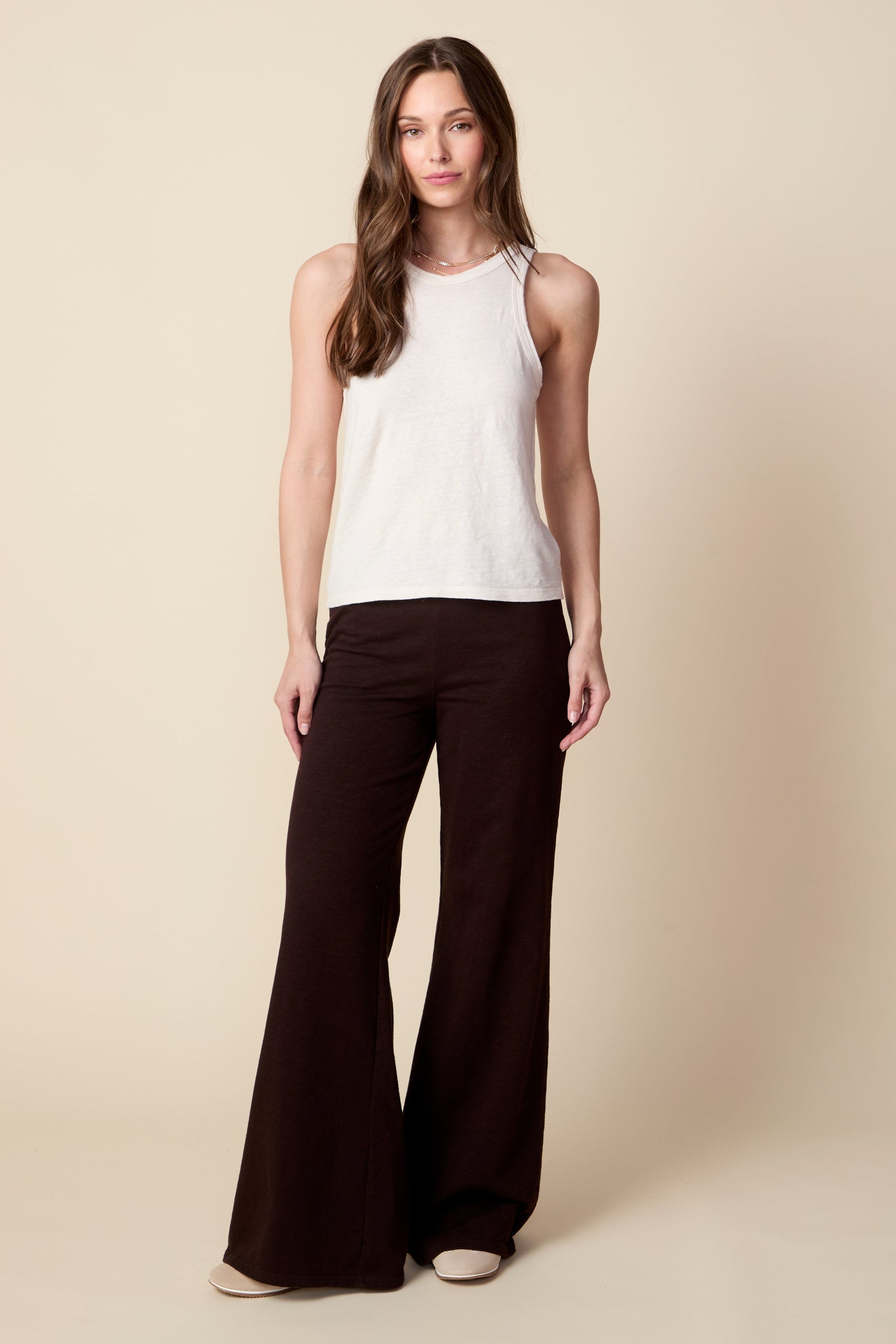 Woman wearing a white sleeveless top and dark brown pants on a beige background