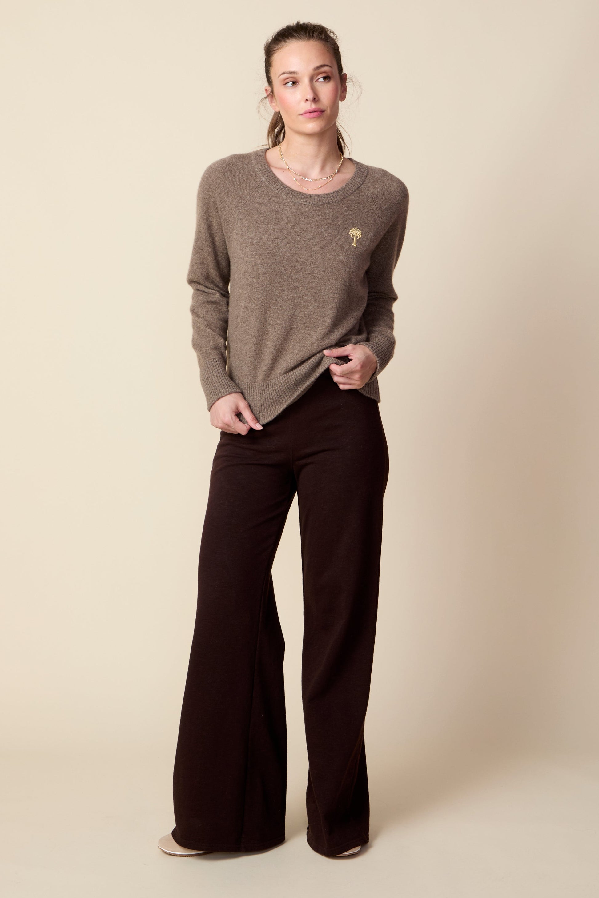Woman wearing a brown sweater and brown pants on a beige background