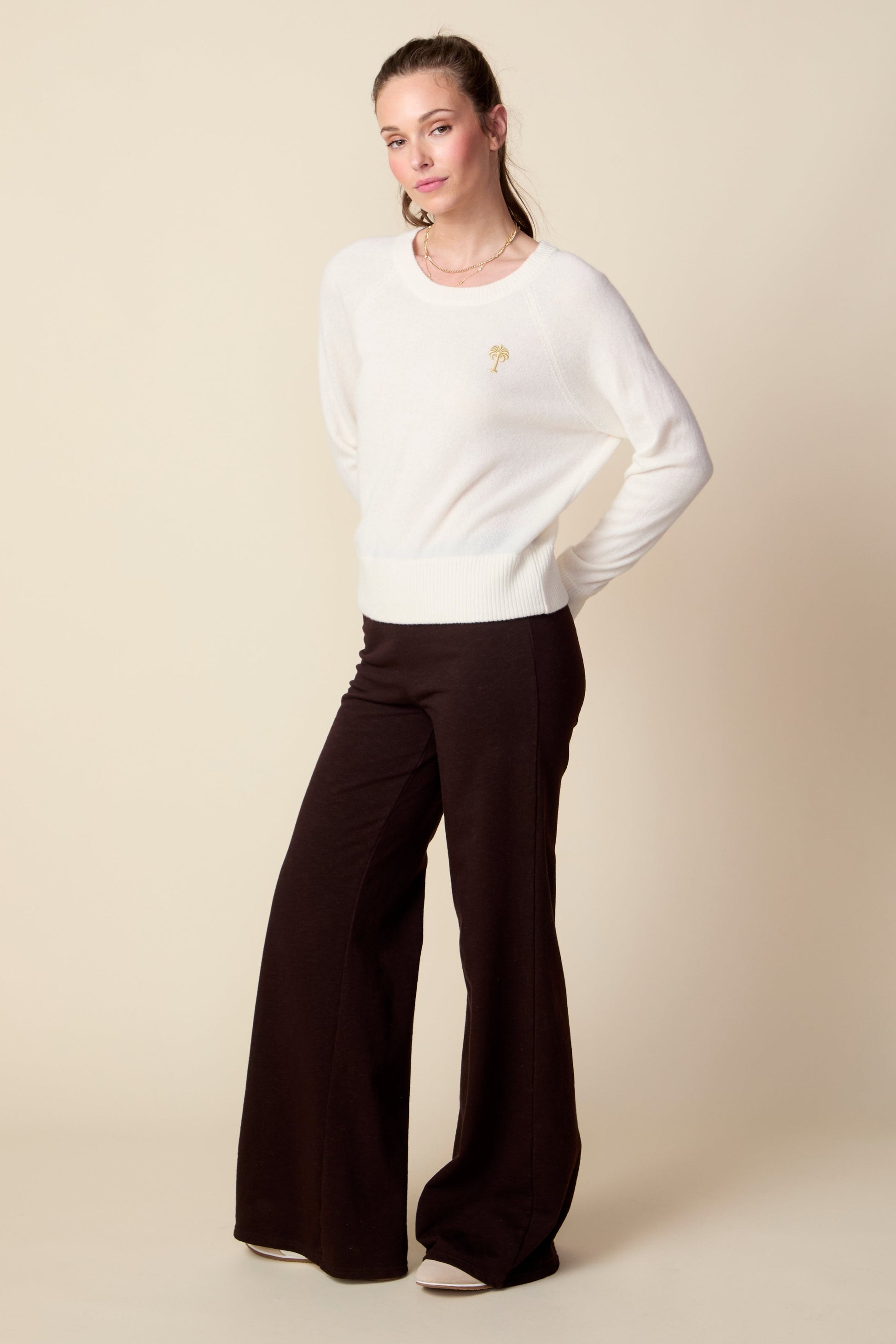 Woman wearing a white sweater and brown pants on a beige background