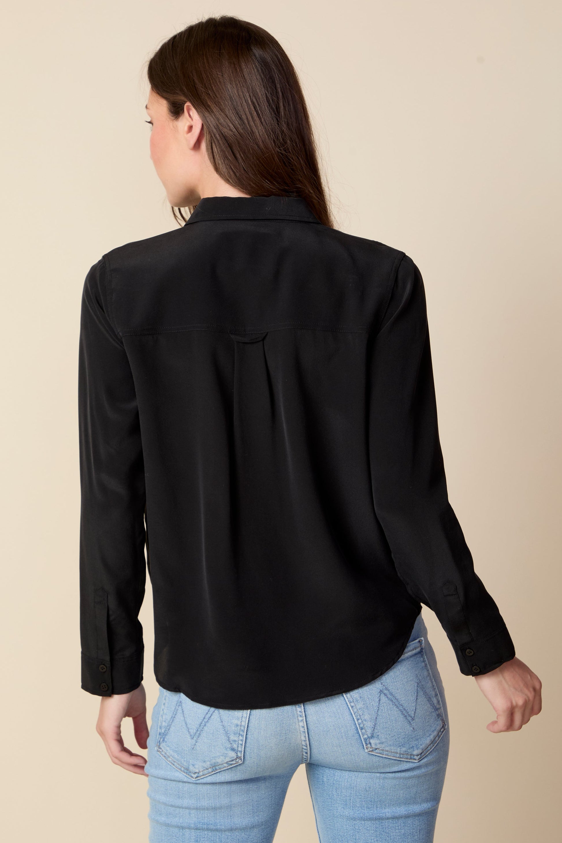 Person wearing a black shirt and light blue jeans on a beige background