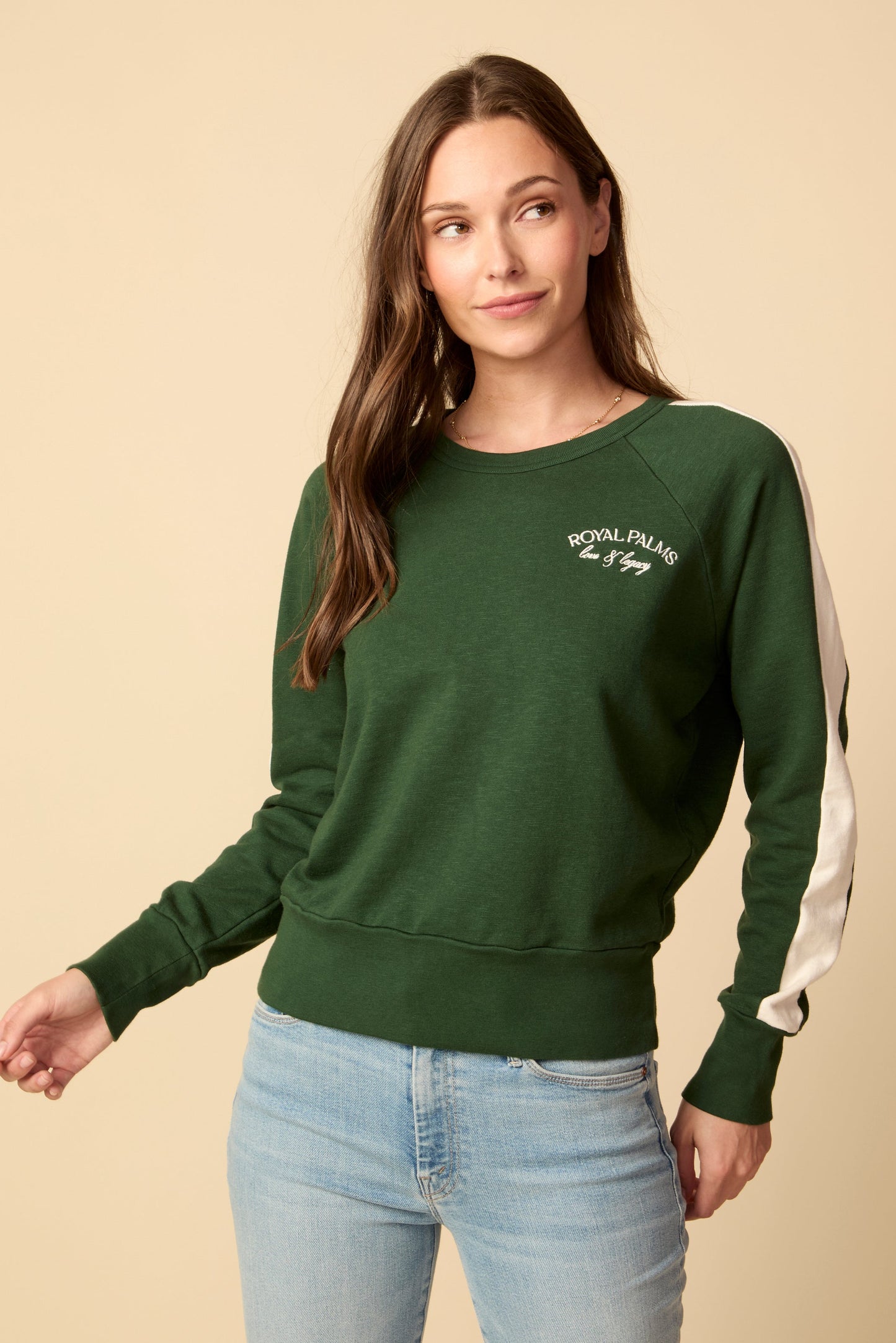 Woman wearing a green sweatshirt with white text and light blue jeans on a beige background