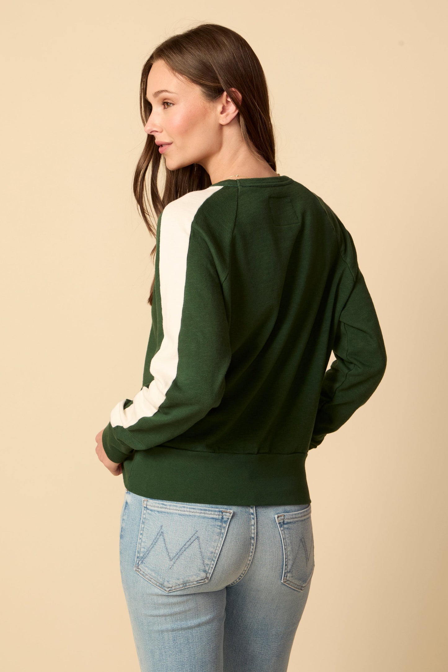 Woman wearing a green and white long-sleeve shirt with light blue jeans on a beige background
