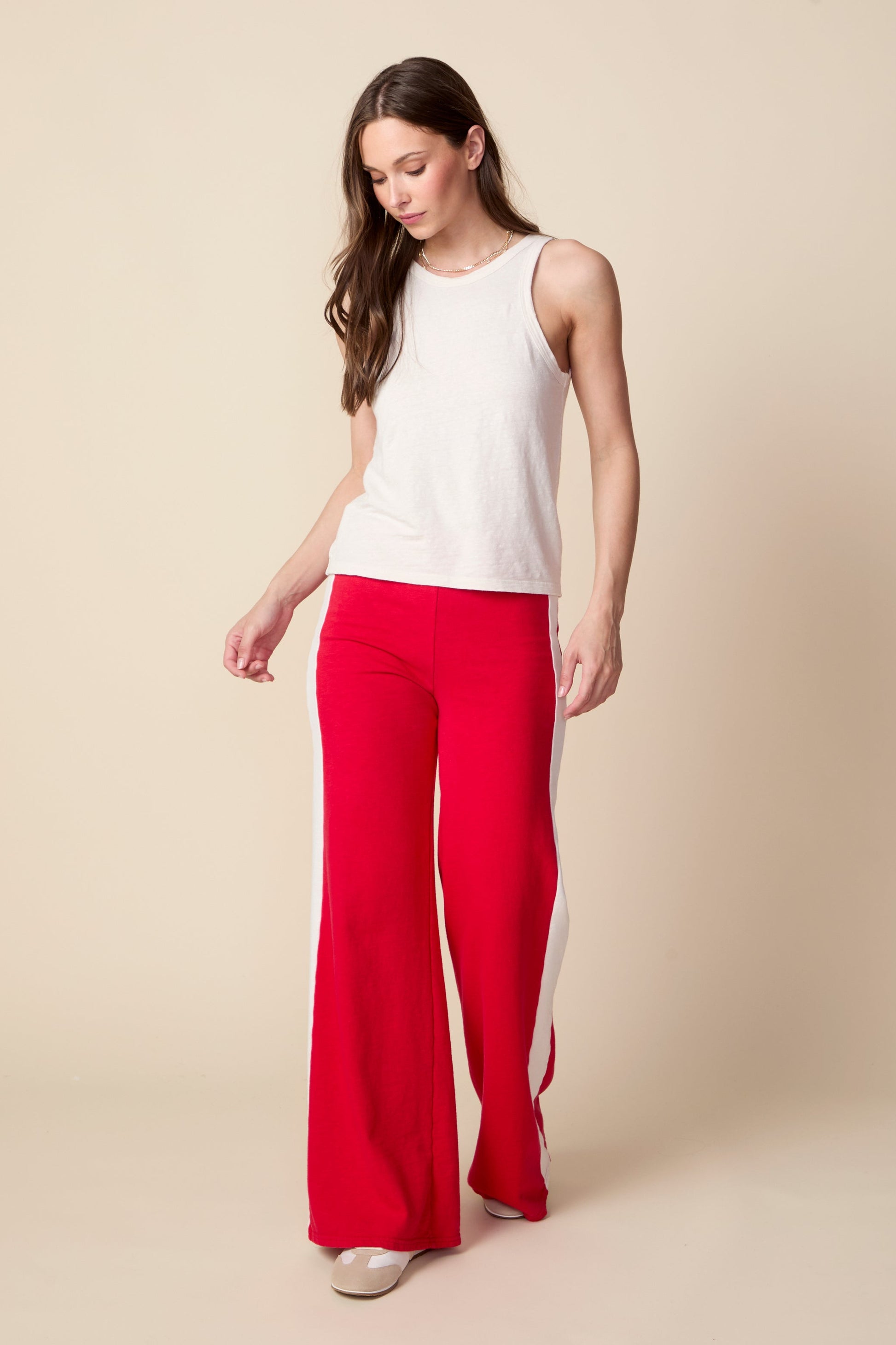 Woman wearing a white sleeveless top and red pants on a beige background