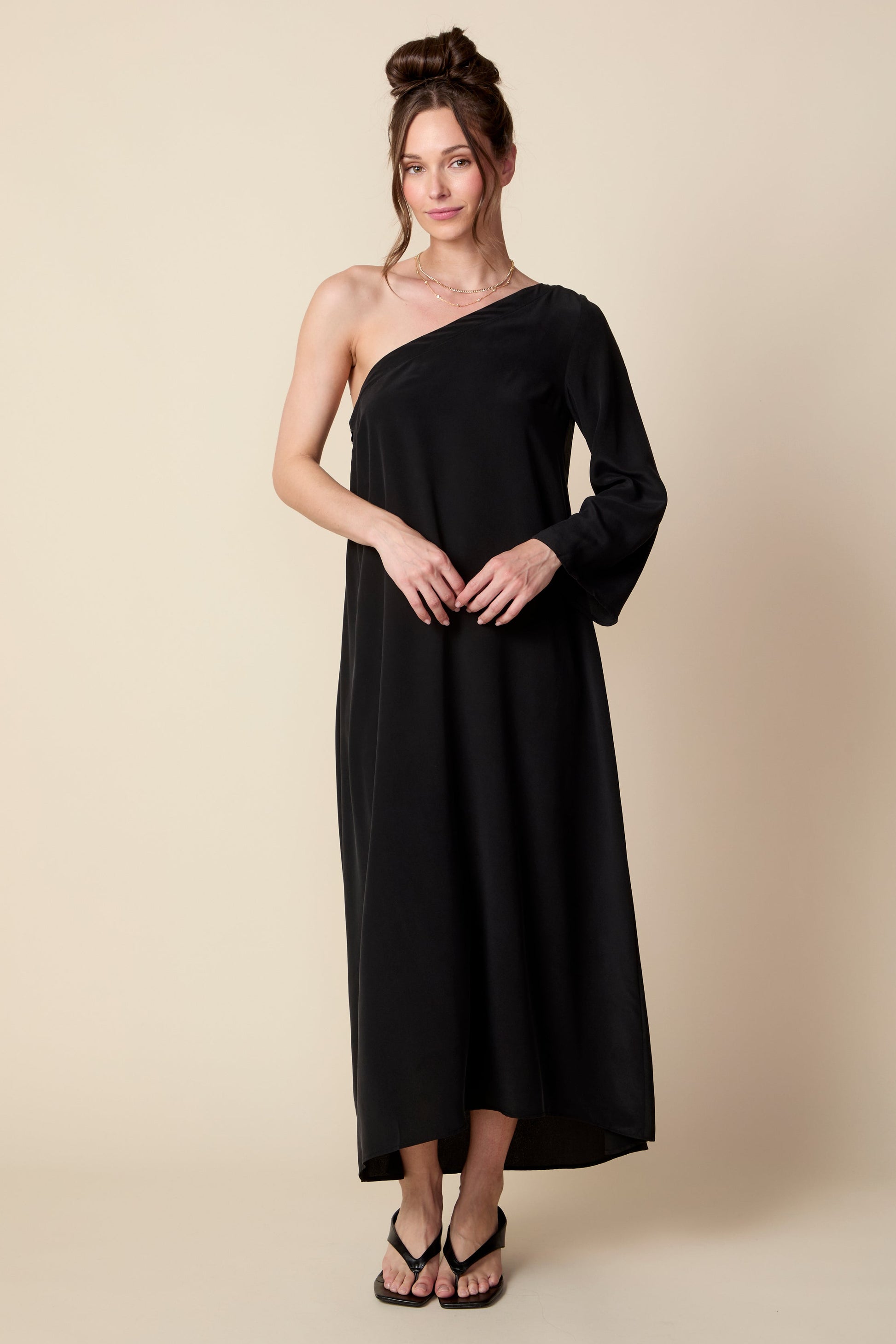 Woman wearing a black one-shoulder dress against a beige background