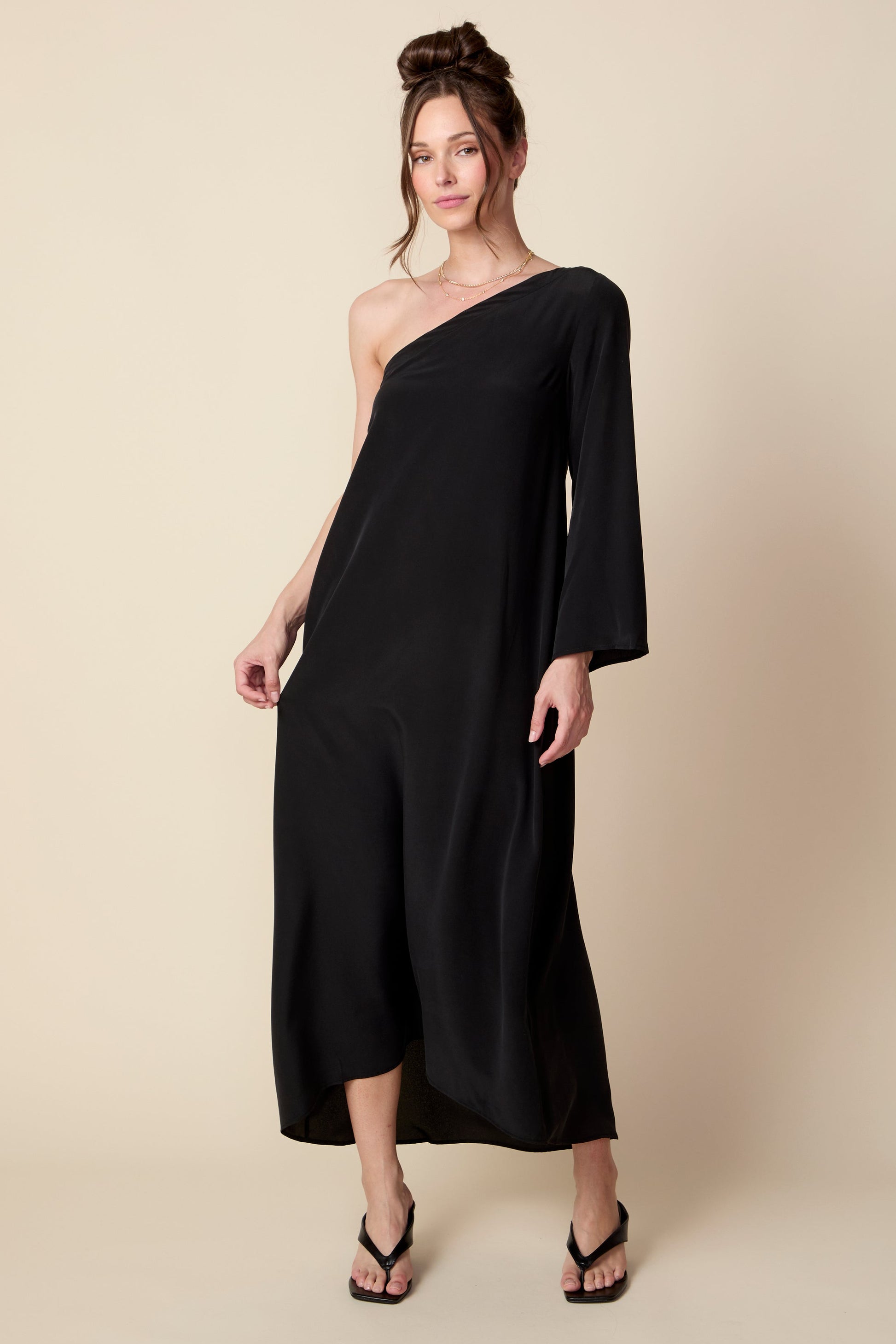 Woman wearing a black one-shoulder dress against a beige background