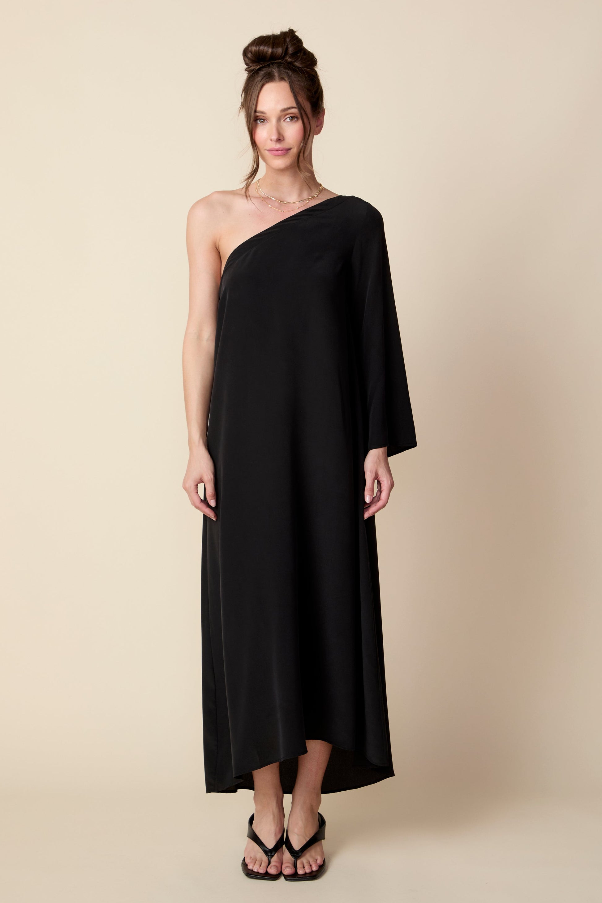 Woman wearing a black one-shoulder dress against a beige background