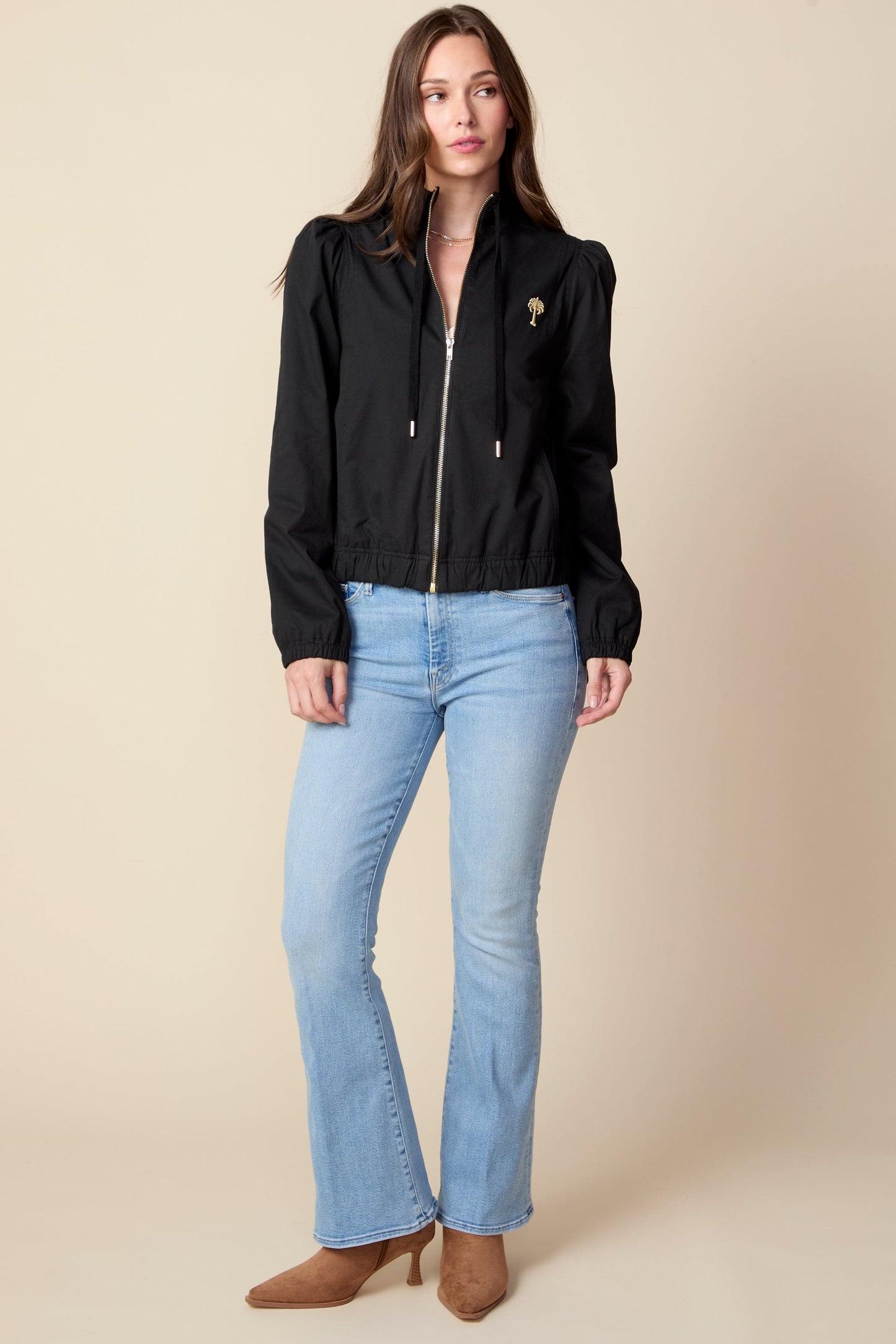 Woman wearing a black jacket and light blue jeans against a beige background