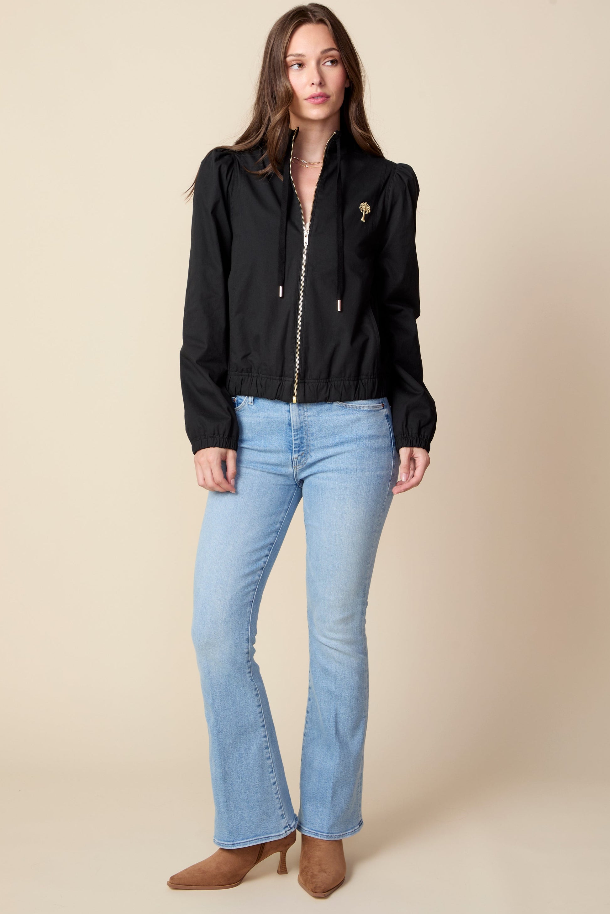Woman wearing a black jacket and light blue jeans against a beige background