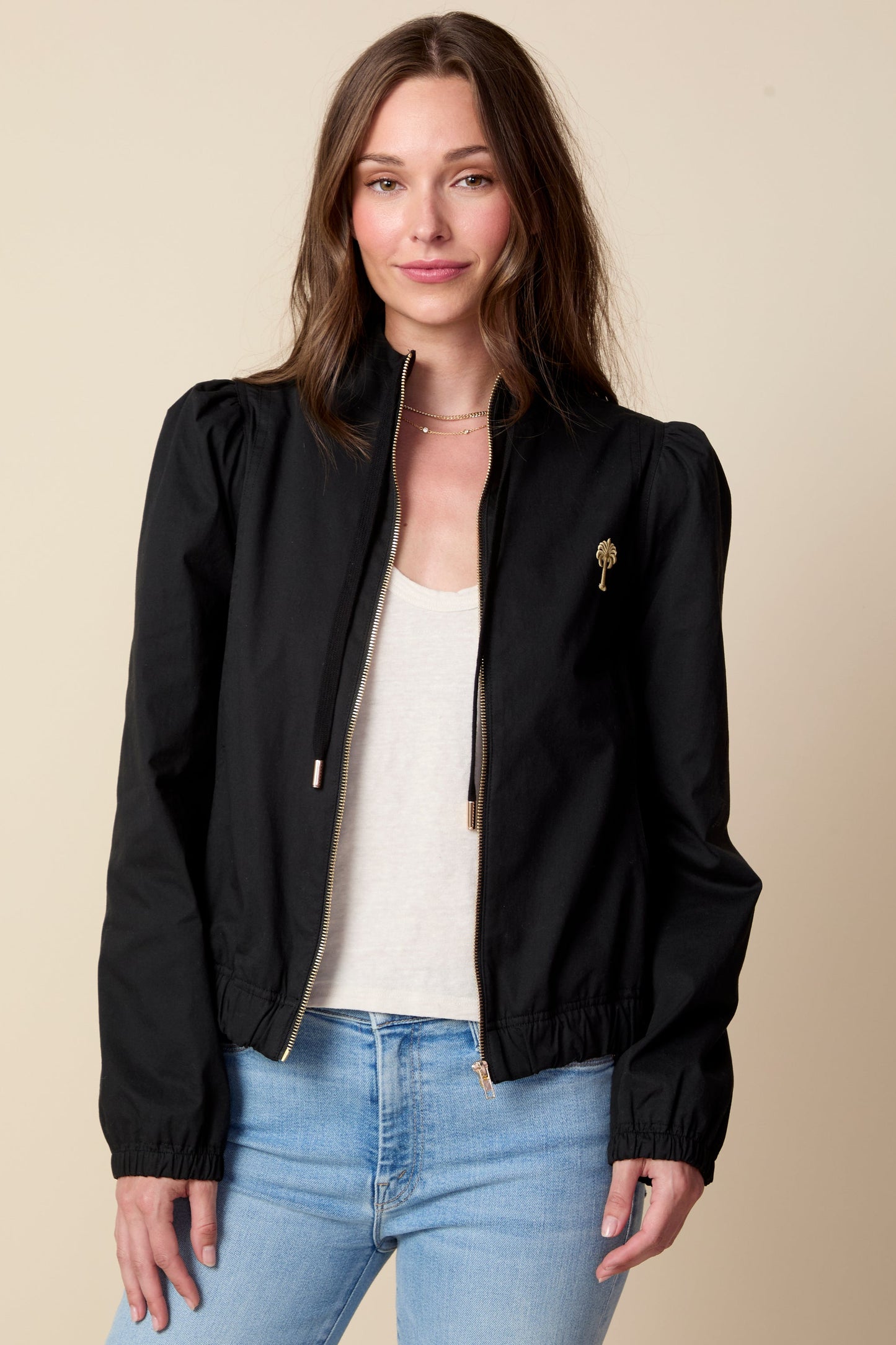 Woman wearing a black jacket and light blue jeans against a beige background