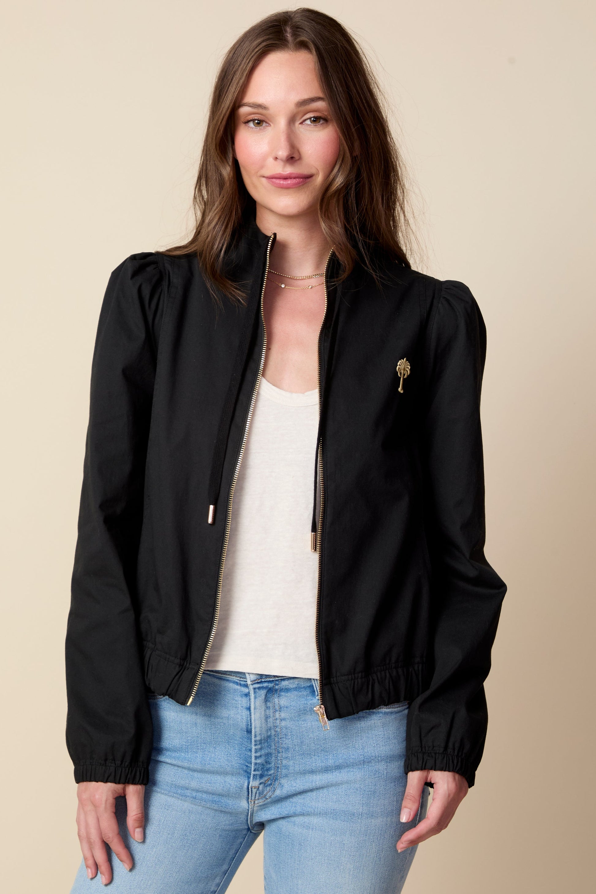 Woman wearing a black jacket and light blue jeans against a beige background