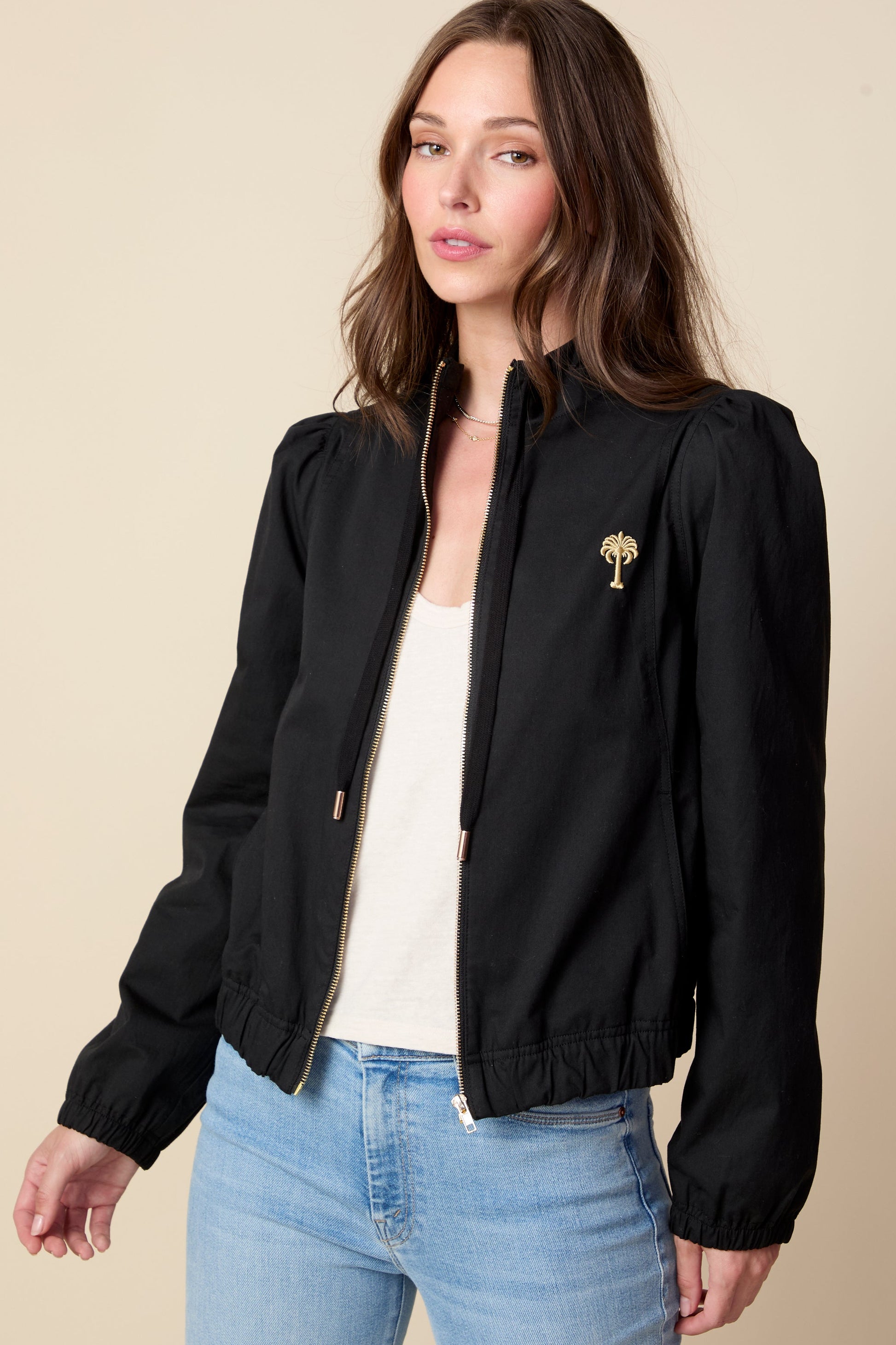 Woman wearing a black jacket with a logo on a beige background