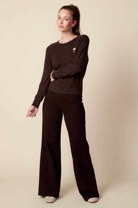 Woman wearing a dark brown sweater and wide-leg pants on a beige background