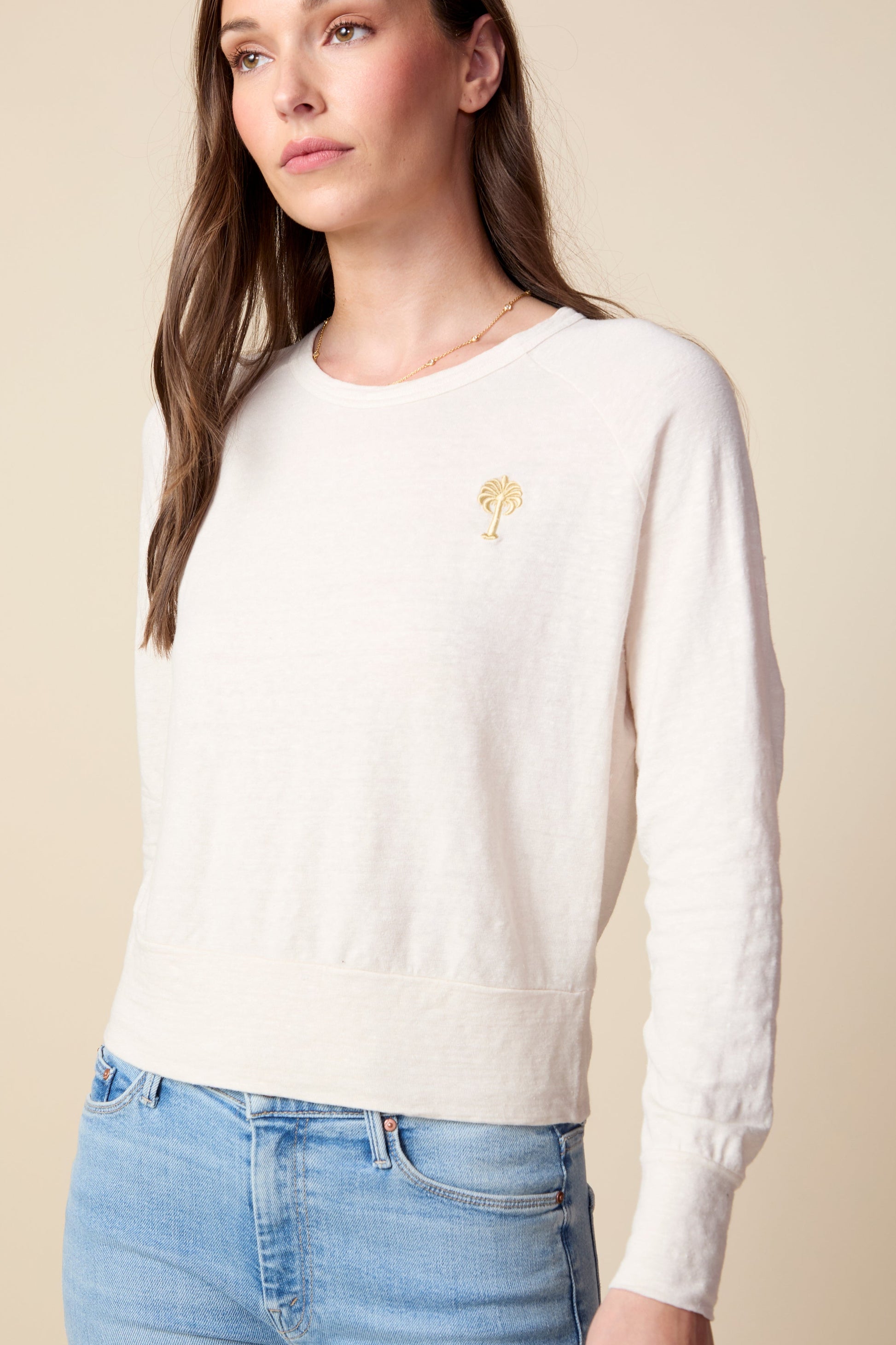 Woman wearing a white sweater with a small embroidered design on a beige background